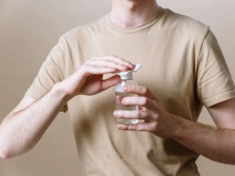 Homem de camiseta bege abrindo um frasco de cuidado com a pele